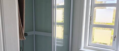 A bathroom with a glass shower enclosure, a window, and a radiator.
