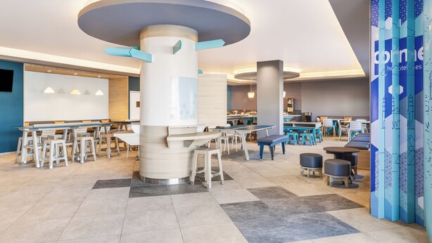 Eine großzügige Lobby mit verschiedenen Sitzbereichen, einer zentralen Säule und einer blauen Dekoration.