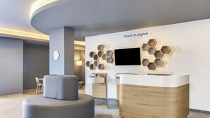 Ein moderner Empfangsbereich mit einer digitalen Check-in-Station, einer Sitzecke und einem wandmontierten Fernseher.