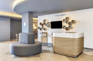 A modern reception area with a digital check-in station, a seating area, and a wall-mounted TV.