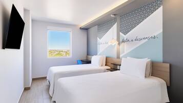 Habitación de hotel con dos camas, televisión, ventana con vistas y pared con un diseño geométrico y texto.
