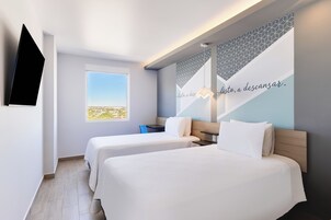 Habitación de hotel con dos camas, televisión, ventana con vistas y pared con un diseño geométrico y texto.