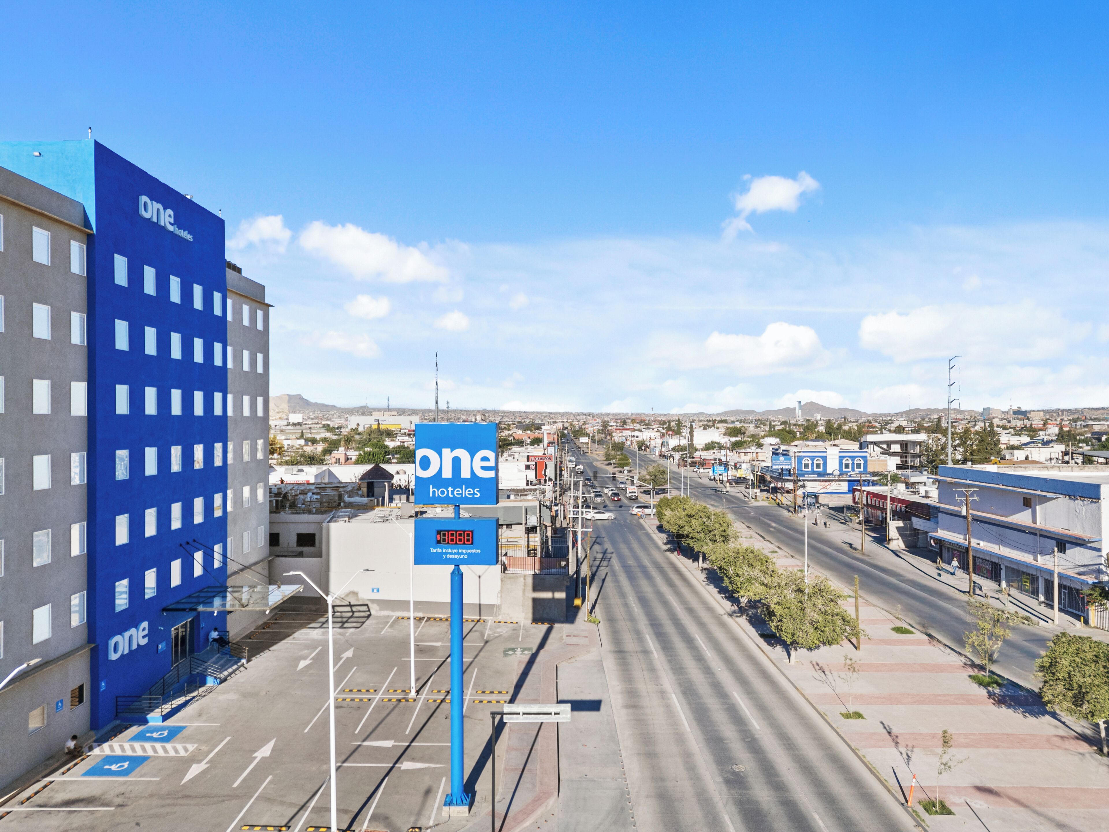A hotel with a blue facade, a parking lot, and a clear view of the surrounding cityscape.