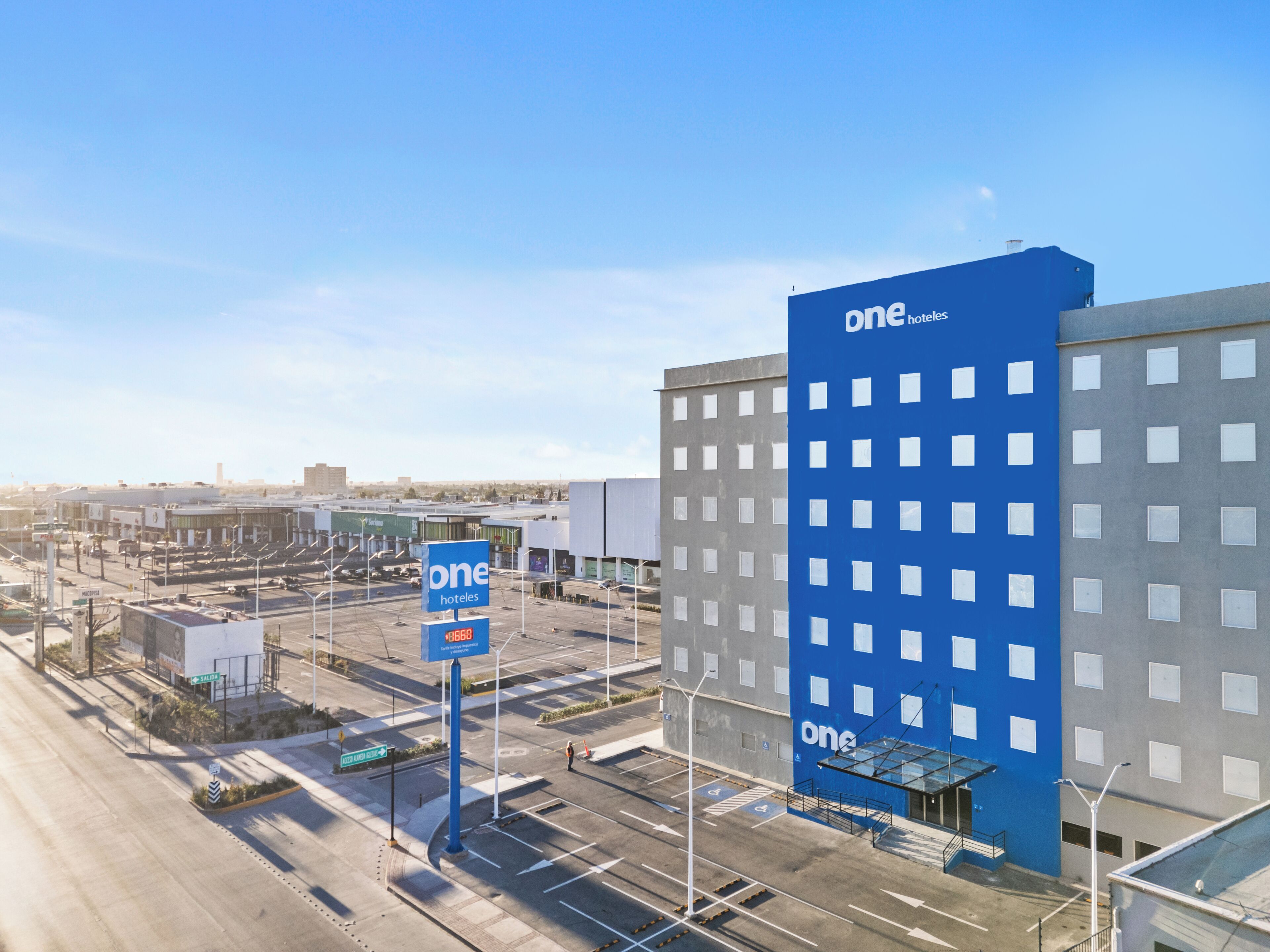 A modern hotel with a blue facade, a parking lot, and clear signage for the hotel.