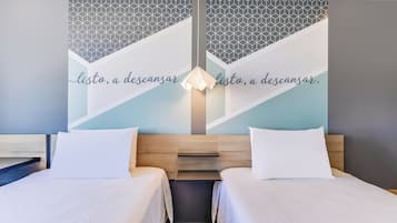 Habitación de hotel con dos camas, un diseño geométrico en la pared y una lámpara.