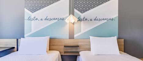Une chambre d’hôtel avec deux lits, un motif géométrique sur le mur et un luminaire.