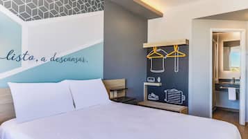 Una habitación de hotel con una cama, un perchero en la pared y un baño a la vista a través de una puerta abierta.