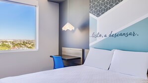 Ein modernes Hotelzimmer mit Bett, Schreibtisch, Stuhl und Blick auf die Stadt.