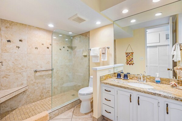 A bathroom with a glass-enclosed shower, a white toilet, a sink with a granite countertop, and a large mirror.