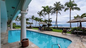 Piscina con vistas al océano, rodeada de palmeras y zonas de estar al aire libre.