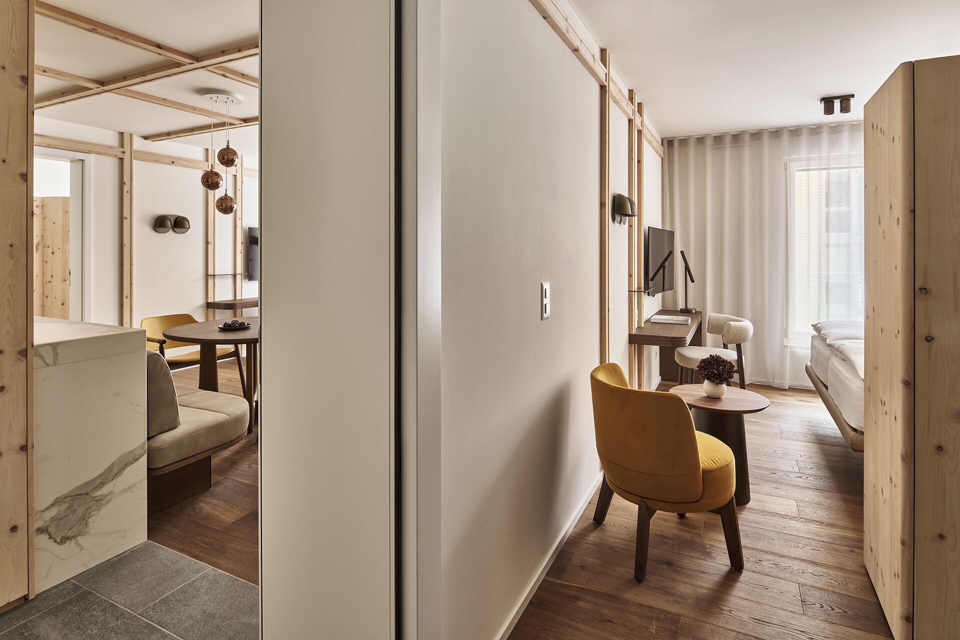 Un interior moderno con piso de madera, una zona de comedor con una mesa redonda y sillas, un sofá y una cama con cabecera.