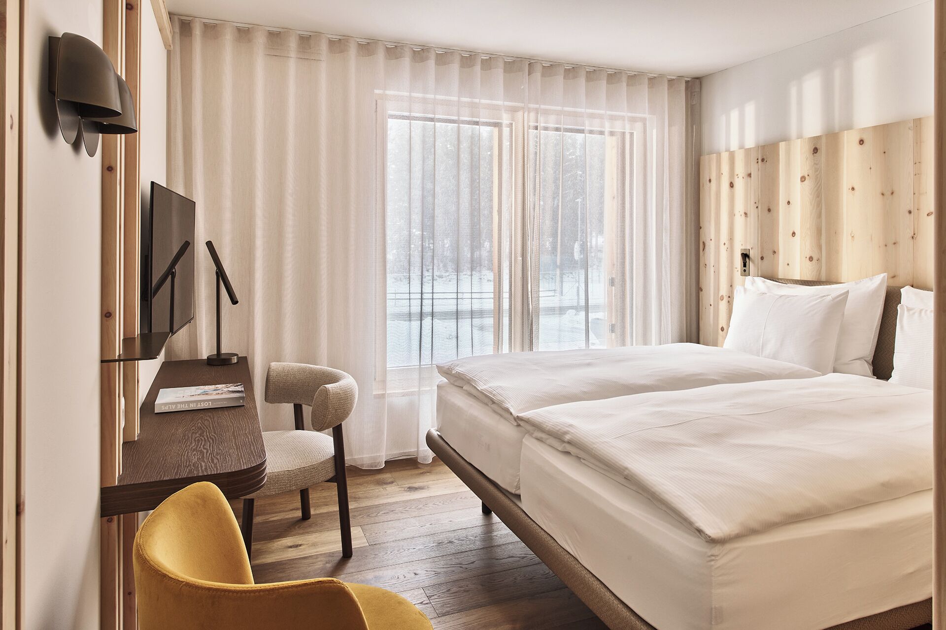 Habitación de hotel con cama, escritorio, silla, televisor y ventana con cortinas.