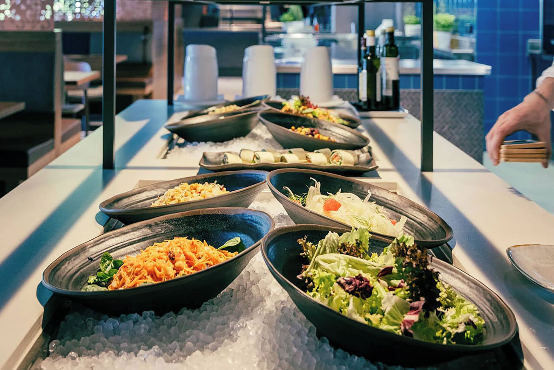 Un bufé con diversos platos, incluyendo ensaladas, pasta y otros alimentos ya preparados, servidos sobre una mesa con hielo.