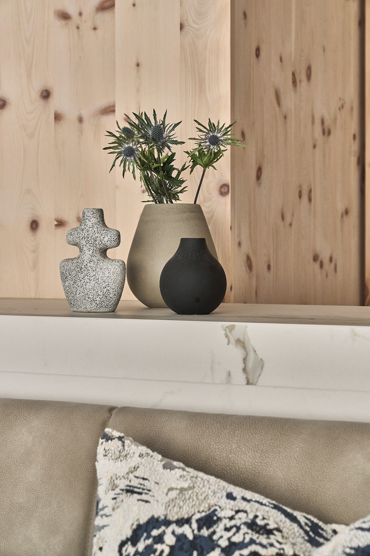 A wooden shelf with three ceramic vases and a plant.