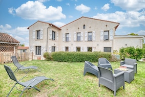 A two-story house with a garden, outdoor furniture, and a wooden fence.