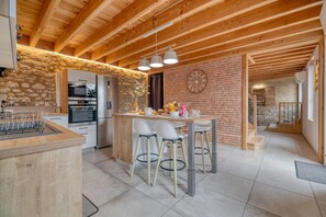 Una cocina moderna con pared de piedra, vigas de madera y una isla central con taburetes de bar.