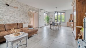 A living room with a stone wall, a brown sofa, a white coffee table, and a dining area with a table and chairs. - Holiday Home 'Les Echaunes' with Private Terrace, Wi-Fi and Air Conditioning (Caraman)