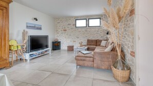 A living room with a stone wall, a sofa, a TV, and a fireplace. - Holiday Home 'Les Echaunes' with Private Terrace, Wi-Fi and Air Conditioning (Caraman)
