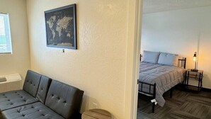 A room with a sectional sofa, two round metal trash bins, a world map on the wall, and a bed with a gray bedspread. - Country Railroad - Wyoming Primo Managment (Green River)