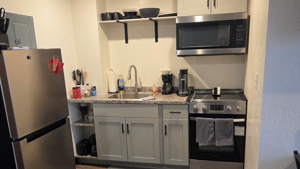 A compact kitchen with a refrigerator, microwave, stove, and cabinets. - Country Railroad - Wyoming Primo Managment (Green River)