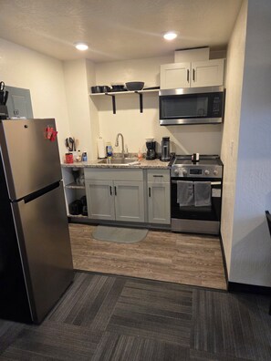 A compact kitchen with a refrigerator, microwave, stove, and cabinets.