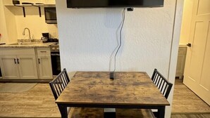 A dining area with a wooden table and chairs, a flat-screen TV mounted on the wall, and a kitchen in the background. - Country Railroad - Wyoming Primo Managment (Green River)