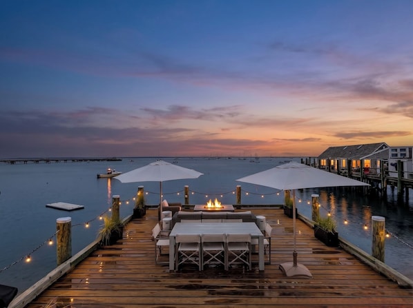 A wooden deck with tables and chairs, a fire feature, and umbrellas.