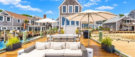 A waterfront property with a wooden deck, outdoor seating, and a view of the beach.