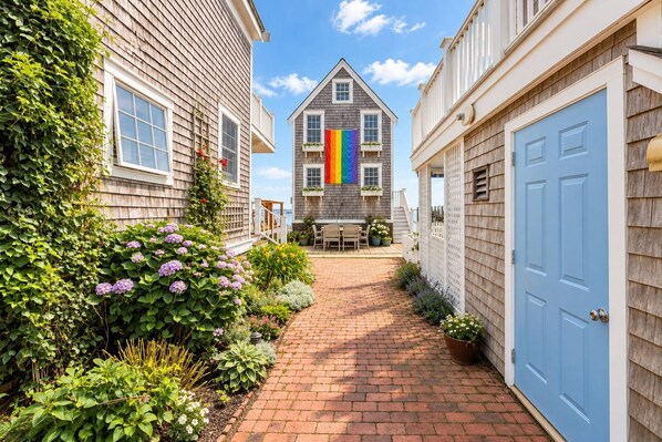 A narrow brick pathway leading to a house with a rainbow flag.