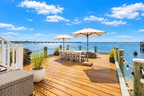 A wooden deck with outdoor furniture, potted plants, and a view of the water.