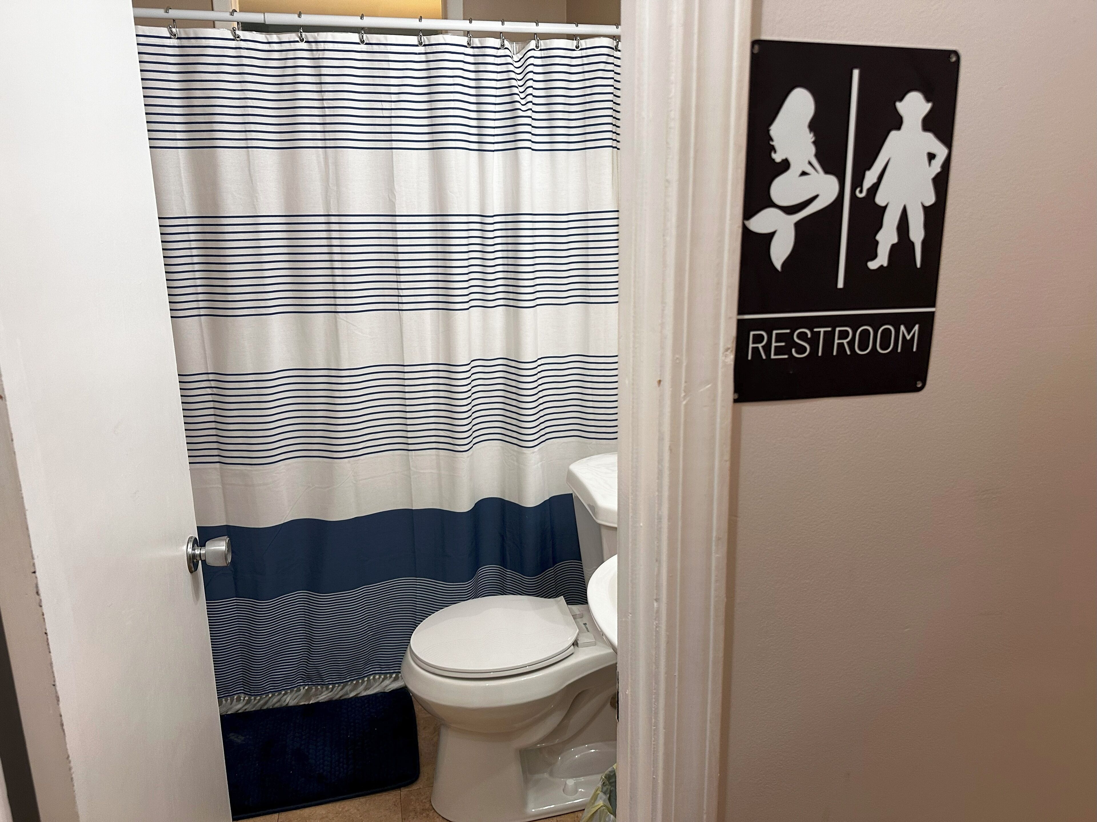 Une salle de bain avec un rideau de douche à rayures, des toilettes et un panneau indiquant les toilettes.