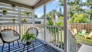 A covered porch with two black wicker chairs, a small table, and potted plants.