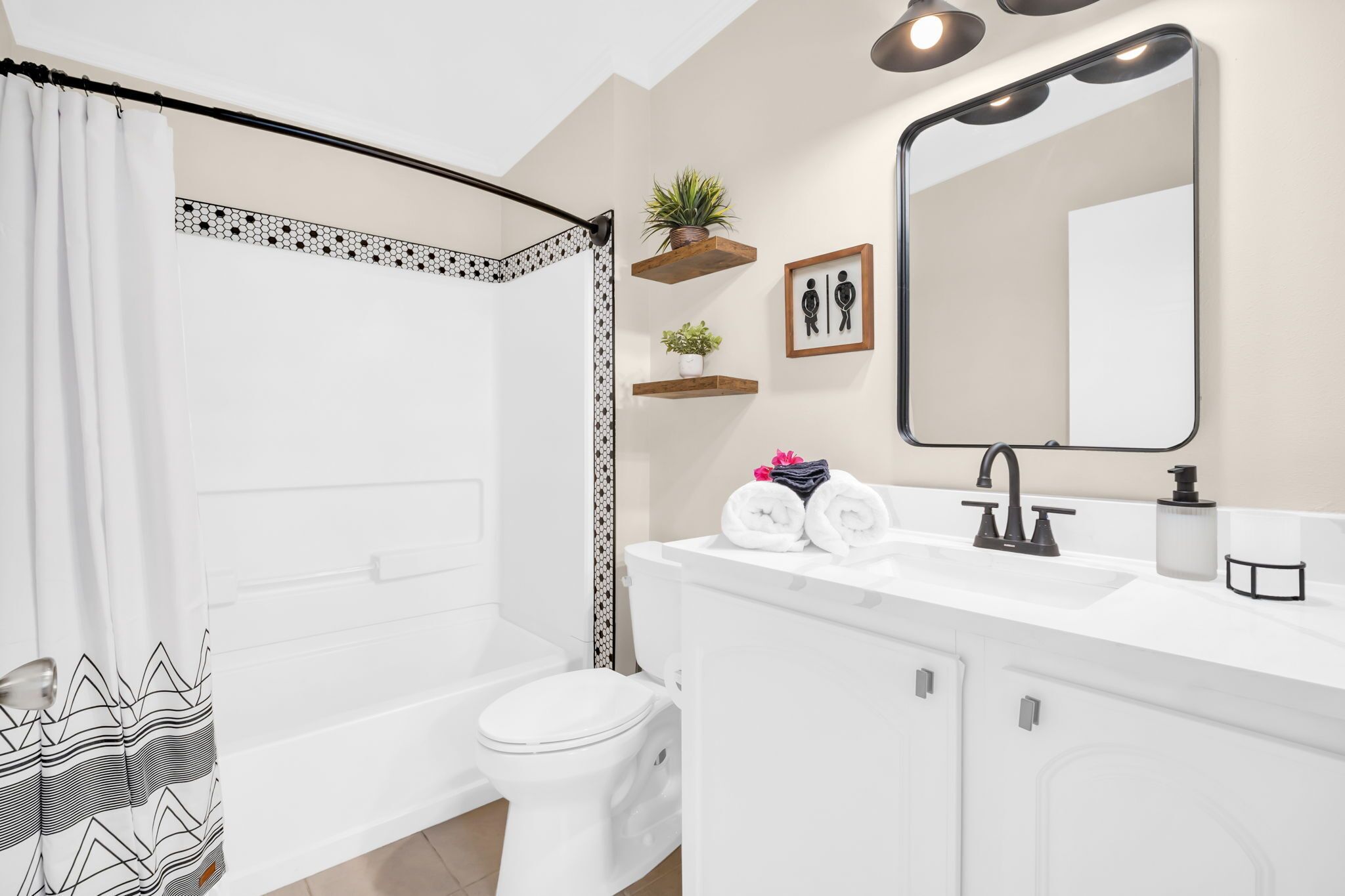 Een moderne badkamer met douchegordijn, toilet, wastafel met spiegel, en twee wandplanken met planten.