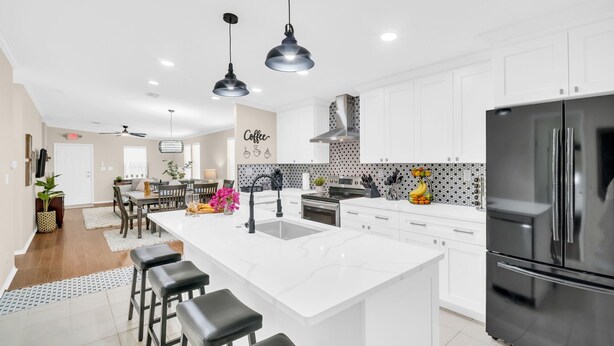 A modern kitchen with white cabinetry, a large island with bar stools, a stainless steel refrigerator, and pendant lighting.