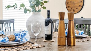 A dining table set with a wine bottle, two salt and pepper shakers, a vase with green foliage, and a clock on the wall.
