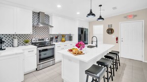 A modern kitchen with white cabinets, a central island with bar stools, stainless steel appliances, and a decorative backsplash.