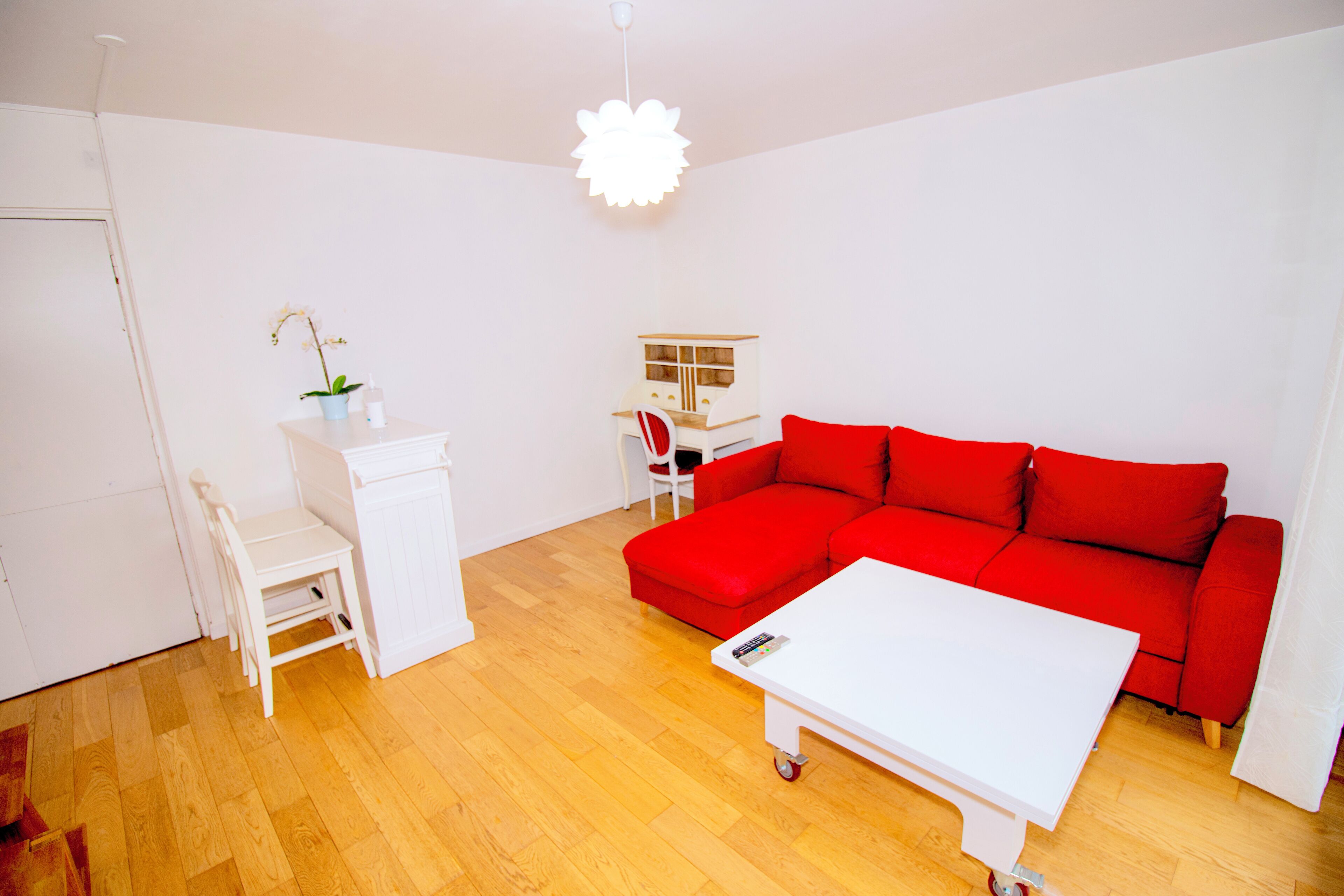 Een moderne woonkamer met een rode bank, een witte salontafel, een wit bureau met stoel en een kleine plant.