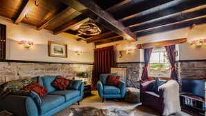 A cozy living room with a stone wall, wooden beams, a fireplace, and a television.