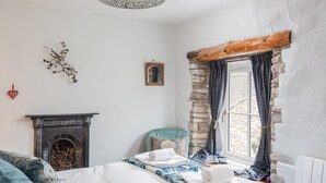 A cozy bedroom with a fireplace, a stone wall, and a window with curtains.