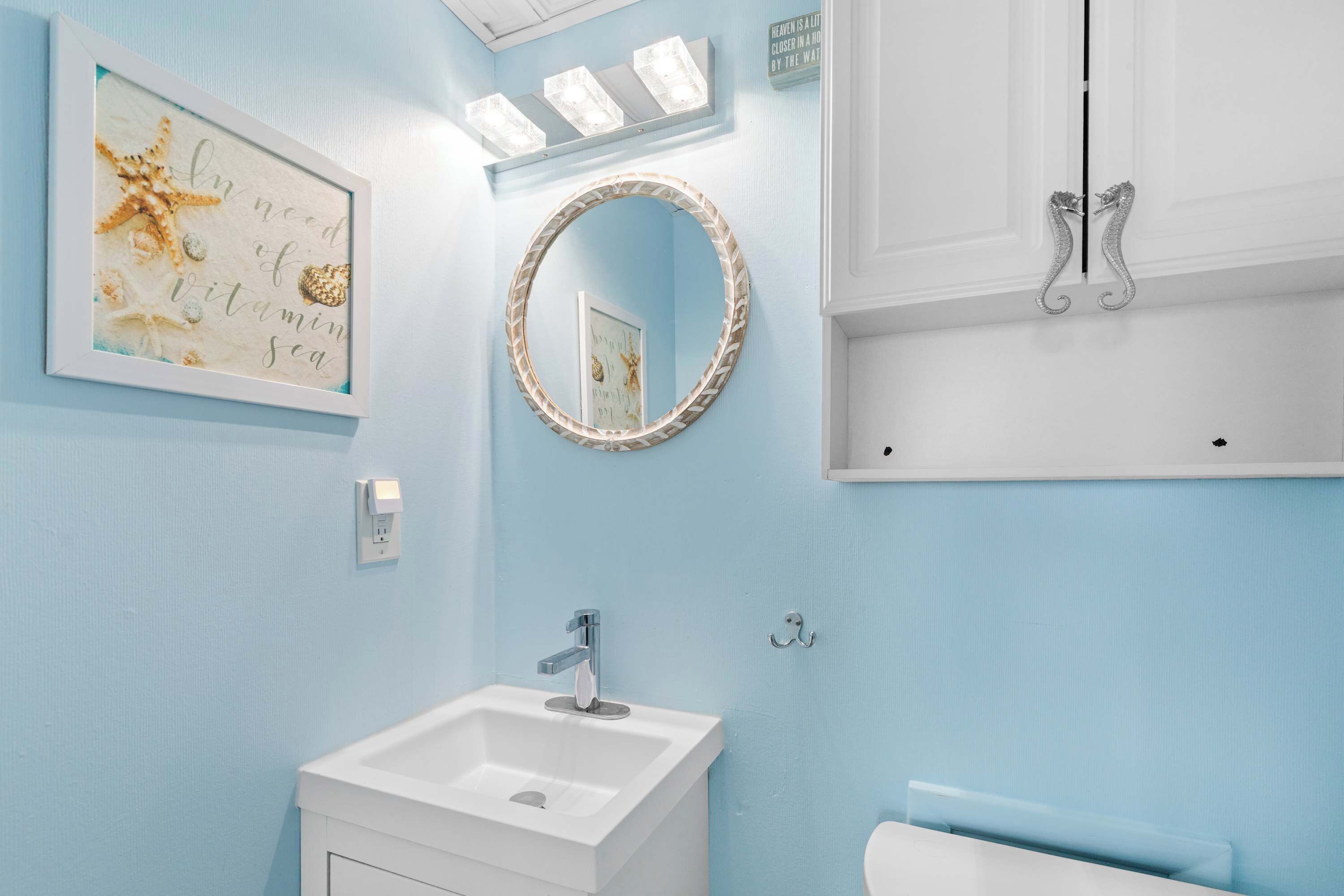 Un bagno con un lavandino bianco, uno specchio tondo con cornice decorativa e un faretto a parete.