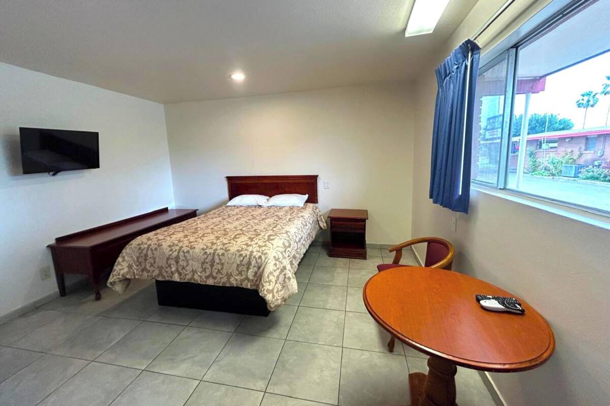 A bedroom with a bed, bedside table, chair, and a small table with a remote control.