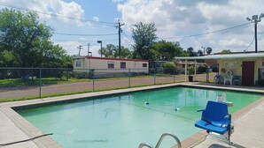 Una piscina con una silla azul, una escalera y una zona cubierta con sillas y un letrero.