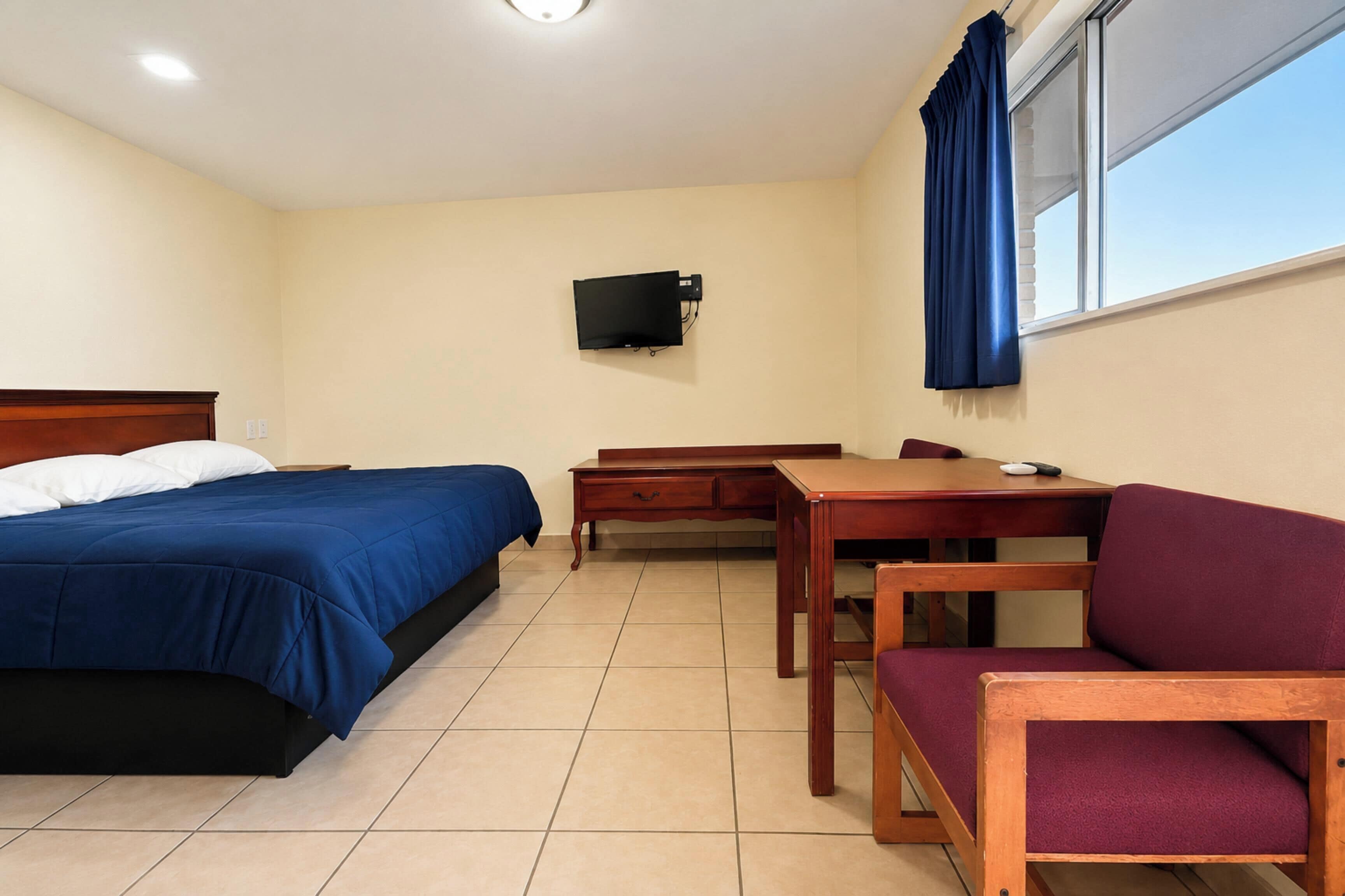 Una habitación con cama, escritorio, silla, televisor y ventana con cortinas.