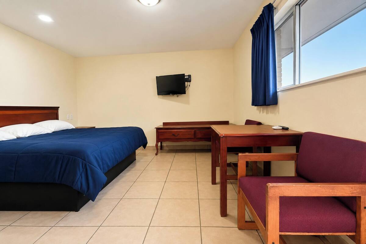 A room with a bed, a desk, a chair, a television, and a window with curtains.