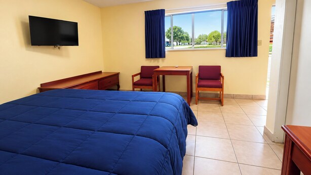 Habitación de hotel con una cama grande, un escritorio, dos sillas, un televisor y una ventana con cortinas.