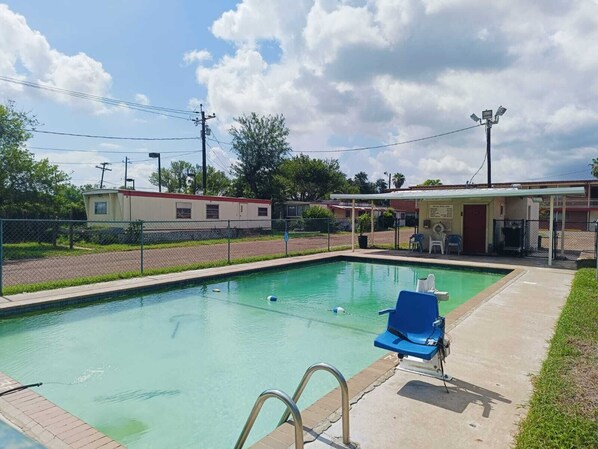 Una piscina con una silla de descanso azul, un área de estar techada y un perímetro cercado.