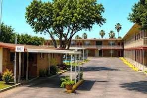 A motel with a covered parking area, a large tree, and a pool.
