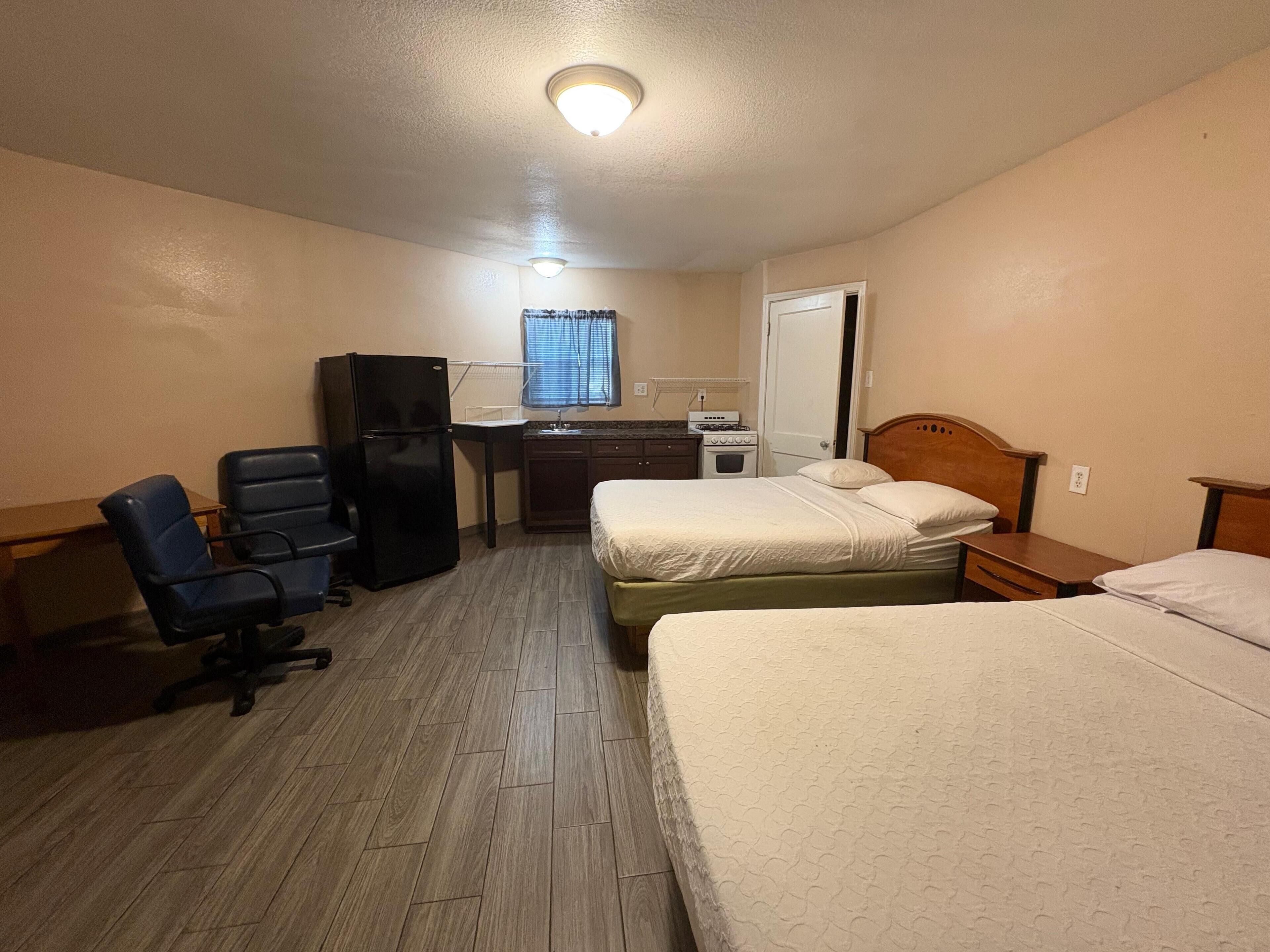 Une chambre d’hôtel avec deux lits, un bureau doté d’un réfrigérateur, une chaise et une fenêtre avec des rideaux.