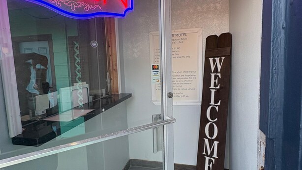 A hotel entrance with a neon 'OPEN' sign, a 'WELCOME' sign, and a glass door. - SE'Air Motel By Townhouse Corpus Christi / Padre Island Tx (Corpus Christi)