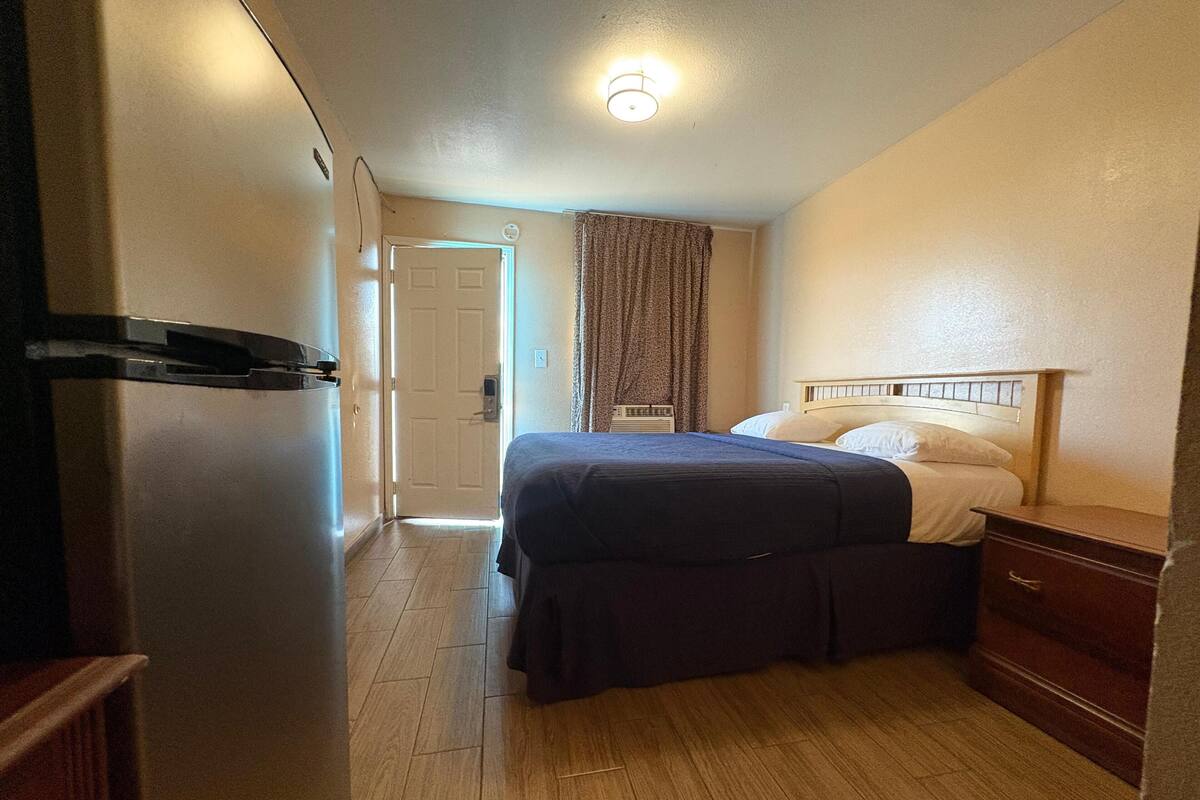 Une chambre d’hôtel avec un lit, une commode, une porte et un luminaire au plafond.